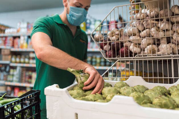 A shopkeeper with a mask taking artichokes from a box in the fruit shop. Torredelcampo, AL, Spain CR_NNSU200920A-508791-01 ,model released, Symbolfoto ,property released