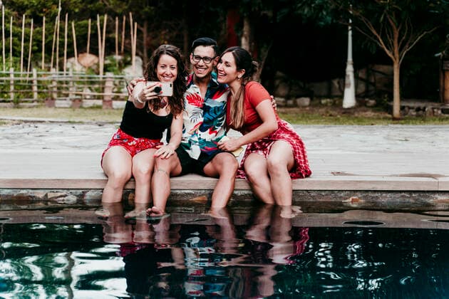 Smiling friends taking selfie while sitting at pool side model released Symbolfoto property released EBBF00732