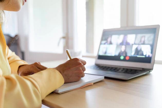 Cropped hands of female entrepreneur writing on diary while talking with colleagues through video conference at home model released Symbolfoto property released AFVF07054
