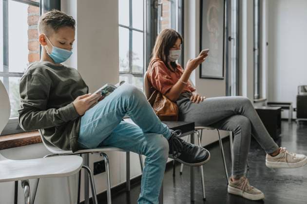 Boy and teenage girl wearing masks sitting on chairs in waiting room model released Symbolfoto property released MFF06118