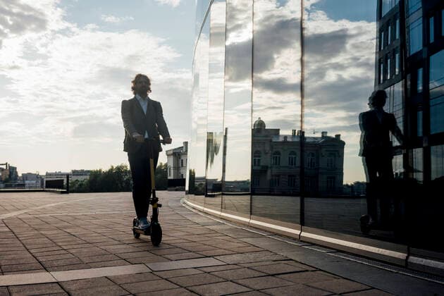 IMAGO Creative: Städte im Wandel Young male commuter riding electric push scooter by modern office building in financial district model released Symbolfoto VPIF02965