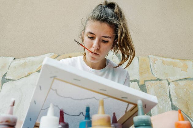white girl biting a bush while painting with her finger her picture in front of bottle paintings. Overhead horizontal photo Zaragoza, Aragon, Spain CR_RUBO200930A-510544-01 ,model released, Symbolfoto ,property released
