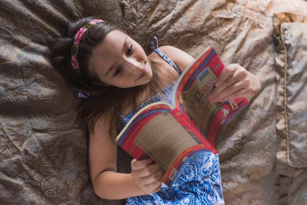 IMAGO Creative: Digitale Welt, Verzicht auf Technologie Smiling girl reading book while lying on bed at home model released Symbolfoto DSIF00137