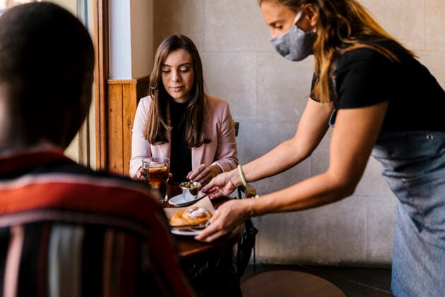 Waitress in protective face mask serving food to young couple at cafe during COVID-19 model released Symbolfoto property released EGAF00883