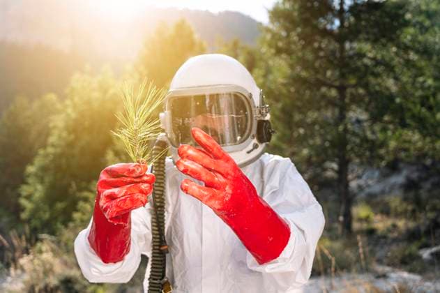 IMAGO Creative: Klimawandel - Zukunft und Innovation Close-up of male astronaut holding plant while standing against trees model released Symbolfoto JCMF01434