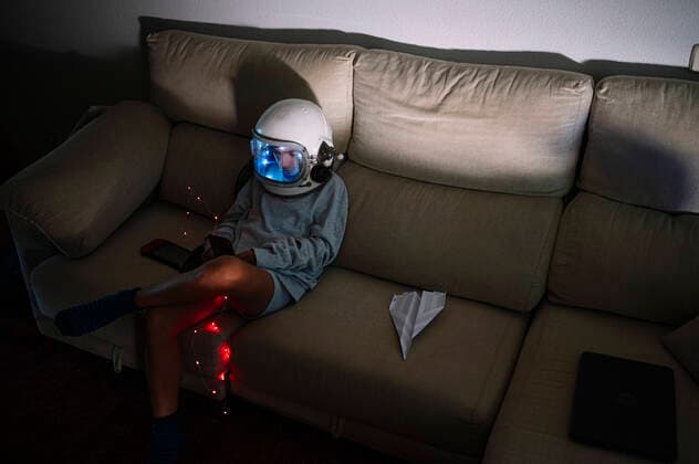 IMAGO Creative: Jahreszeit Winter, Couching Boy wearing space helmet sitting with illuminated lighting equipment on sofa at home model released Symbolfoto property released JCMF01467