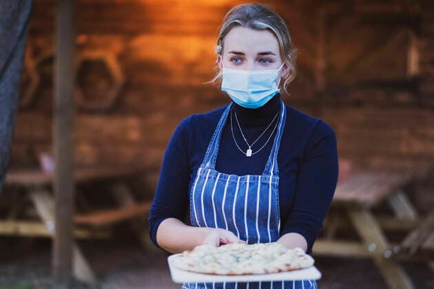 IMAGO Creative: Landleben - Essen Woman waitress in apron and face mask holding fresh pizza on a board Pizza Restaurant,United Kingdom,Woman waitress in apron and face mask holding fresh pizza on a board  Woman waitress in apron and face mask holding fresh pizza on a board