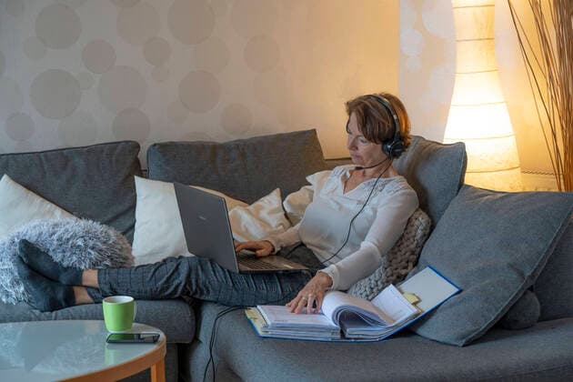 Woman, mid 50s, works from home, with laptop and communicates with colleagues via headset, home office, on the sofa, home office