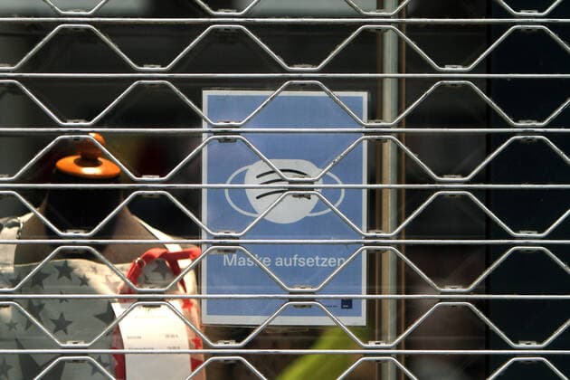 Shield with pictogram Mask duty hangs in the shop window of a shop closed with a roller shutter in the city centre of Cologne, North Rhine-Westphalia, Germany