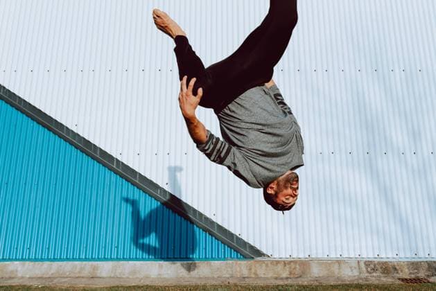 Side view of barefoot guy in stylish outfit performing flip near wall of modern building on city street, Model released Copyright: xAlbertoxMenendezx MR