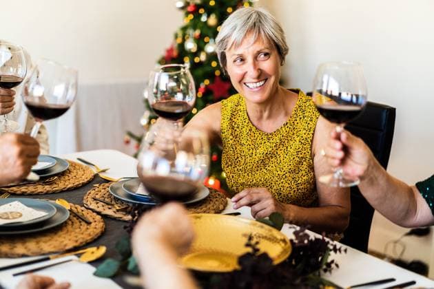 Happy mature friends gathering at festive table near shining Christmas tree and clinking wineglasses while celebrating Christmas eve together, Model released Copyright: xAlvaroxSanchezx MR
