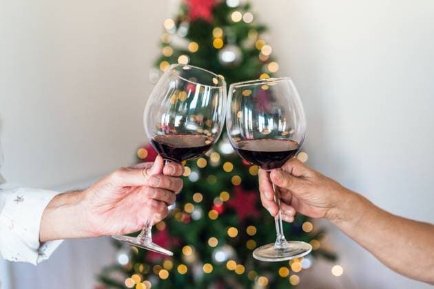 Crop unrecognizable friends with shiny glasses of alcoholic beverage near bright decorative tree during New Year holiday, Model released Copyright: xAlvaroxSanchezx MR