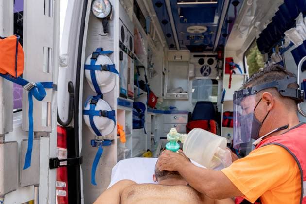 Side view of anonymous male employee in protective shield putting oxygen mask on face of man in ambulance car Copyright: xCarlesxNavarrox Model Released