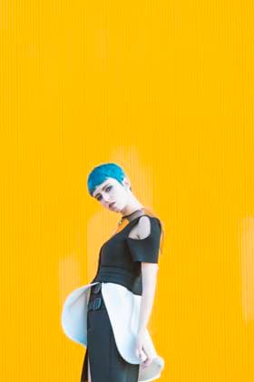 IMAGO Creative: Clickbait, Modetrends Sensual young woman in trendy futuristic dress looking at camera while standing on knees on pavement against bright yellow wall, Model released Copyright: xDavidxAguerox MR
