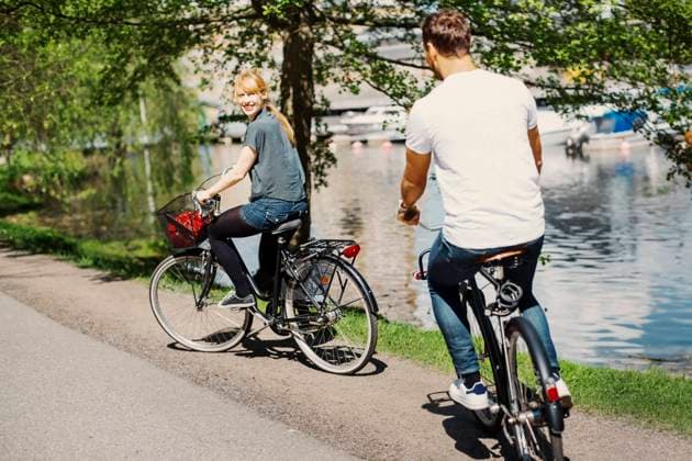 IMAGO Creative, Jahreszeit Sommer, Sommer in der Stadt Happy businesswoman looking at colleague while riding bicycles on street by lake , model released Copyright: xMaskotx , MA45531