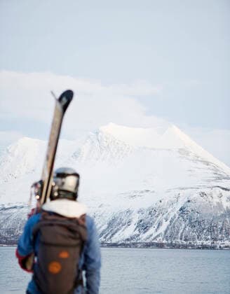 Rear view of man carrying skis looking at river and snow covered mountains , model released Copyright: xKentarooxTrymanx , MA49876