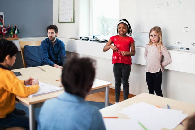 Female students standing against whiteboard wile teacher sitting in classroom , model released, property released Copyright: xMaskotx , MA51276