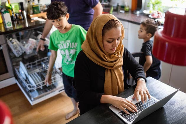 High angle view of woman using laptop on dining table with family working in background at kitchen , model released, property released Copyright: xMaskotx , MA51715