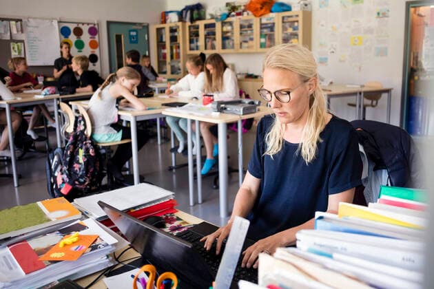 Teacher using laptop on desk with students sitting in classroom , model released, property released Copyright: xMaskotx , MA51966