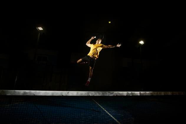 Athletic male holding racket and jumping to kick ball on tennis court in obscurity Copyright: xFranxRosadox Model Released