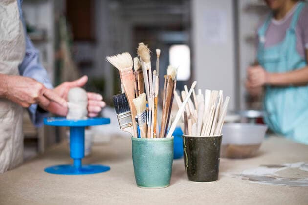 Hand tools and paintbrushes in containers on workbench with female potters working in background , model released, property released Copyright: xMaskotx , MA55864