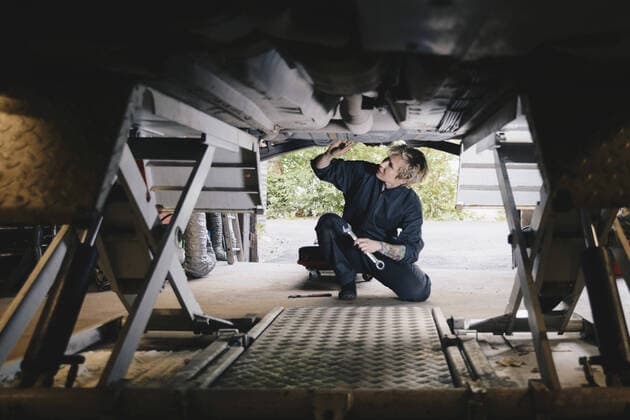 Female mechanic kneeling while examining under car at auto repair shop , model released, property released Copyright: xMaskotx , MA56778