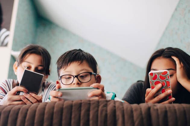 Low angle view of boy looking at digital tablet while lying with sisters using mobile phone on bed at home , model released, property released Copyright: xMaskotx , MA59943