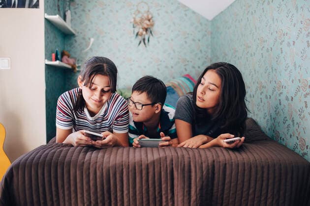 Siblings using wireless technologies while lying on bed by wall at home , model released, property released Copyright: xMaskotx , MA59945