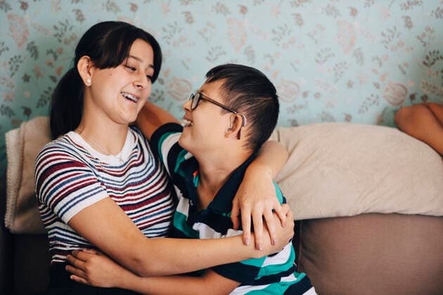 Loving brother and sister embracing on sofa against wall in living room , model released, property released Copyright: xMaskotx , MA59948
