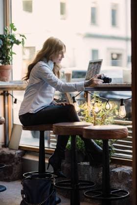 Full length of young woman holding camera while sitting with laptop at cafe , model released, property released Copyright: xMaskotx , MA62157