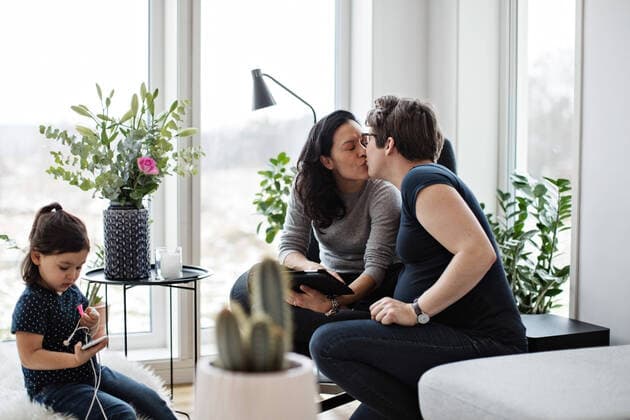 Lesbian couple kissing while girl using mobile phone in living room at home , model released, property released Copyright: xMaskotx , MA63083