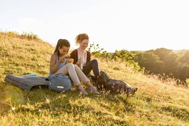 Smiling woman and daughter with insulated drink container sitting on grass at hill against sky during sunset , model released Copyright: xKentarooxTrymanx , MA63494