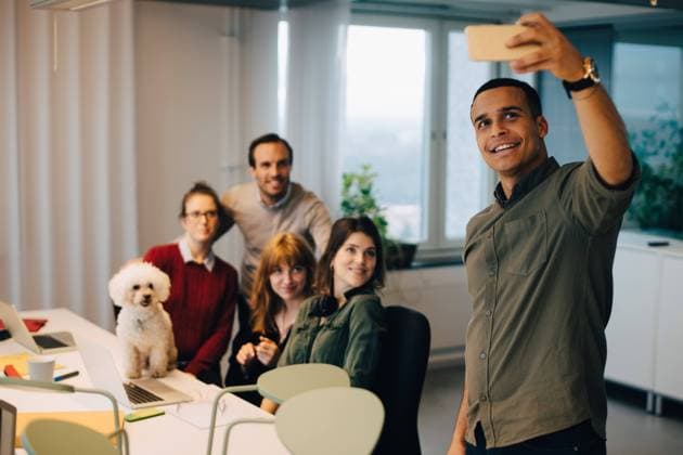 IMAGO Creative, Health, Hunde im Büro reduzieren Stress Smiling businessman taking selfie with colleagues at dog at creative office , model released, property released Copyright: xMaskotx , MA63767