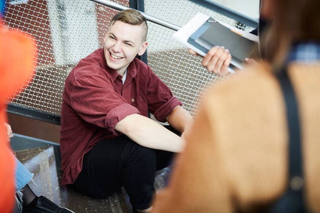 Smiling man sitting on steps while talking to friends in university , model released, property released Copyright: xMaskotx , MA65405