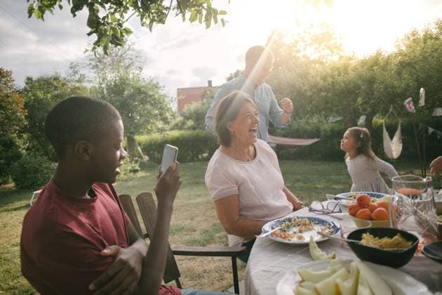 IMAGO Creative: Dichotomien, Generationen Boy photographing cheerful family enjoying lunch at table during garden party , model released, property released Copyright: xMaskotx , MA67048