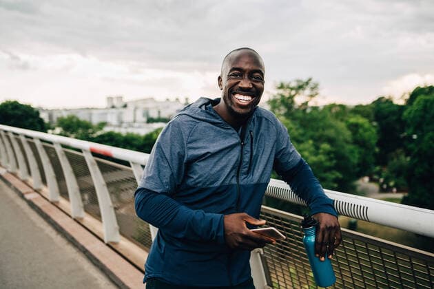 Portrait of cheerful sportsman holding mobile phone and bottle while standing on footbridge , model released Copyright: xMaskotx , MA67300