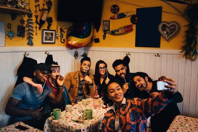IMAGO Creative: Kimawandel - Weihnachten, Weihnachtsessen vegan Young woman taking selfie with cheerful multi-ethnic friends holding props while sitting at restaurant during dinner par , model released, property released Copyright: xMaskotx , MA67351
