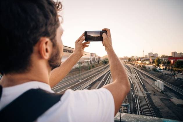 Young man photographing through mobile phone over railroad tracks in city , model released Copyright: xMaskotx , MA67515