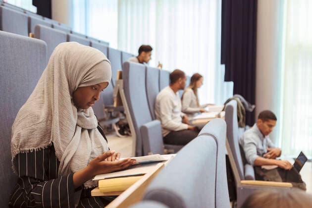 Serious woman in hijab reading book by students at university lecture hall , model released, property released Copyright: xKentarooxTrymanx , MA68350