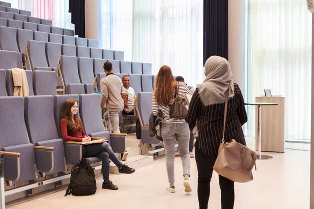 Smiling students looking at friends walking towards chairs in lecture hall at high school , model released, property released Copyright: xKentarooxTrymanx , MA68352
