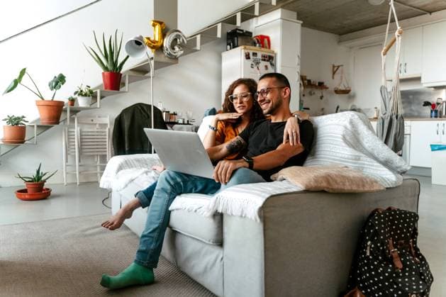 IMAGO Creative: Jahreszeit Winter, Couching Concentrated young female in eyeglasses cuddling ethnic husband while watching movie together on laptop sitting on sofa at cozy home Copyright: xJakexJakabx Model Released