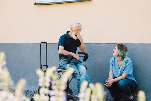 IMAGO Creative: Zivildienst und ehrenamtliches Engagement Smiling female nurse looking at senior man playing harmonica against wall at back yard , model released, property released Copyright: xMaskotx , MA68866
