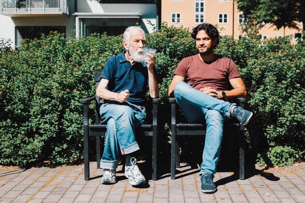 IMAGO Creative: Zivildienst und ehrenamtliches Engagement Full length of retired senior man smoking pipe while sitting with male caretaker against nursing home , model released, property released Copyright: xMaskotx , MA68878