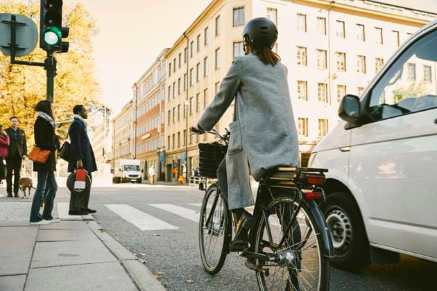 IMAGO Creative: Klimawandel - Zukunft und Innovation Rear view of woman riding electric bicycle by car on street in city , model released Copyright: xMaskotx , MA69570