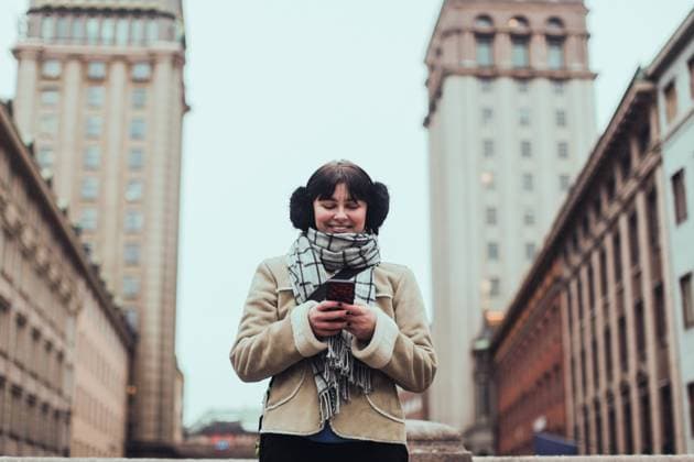 IMAGO Creative, Jahreszeit Winter in der Stadt IMAGO Creative: Winter in der Stadt Smiling young woman wearing warm clothing while using mobile phone against buildings in city , model released Copyright: xMaskotx , MA69983