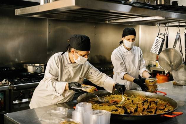 Focused female chefs placing delicious noodle with seafood in plastic container for delivery while working in restaurant kitchen during coronavirus pandemic Copyright: xJavierxBallesterx Model Released