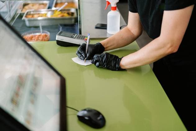 Unrecognizable waiter wearing face mask and gloves taking notes on paper while working at cafe counter during coronavirus pandemic Copyright: xJavierxBallesterx Model Released