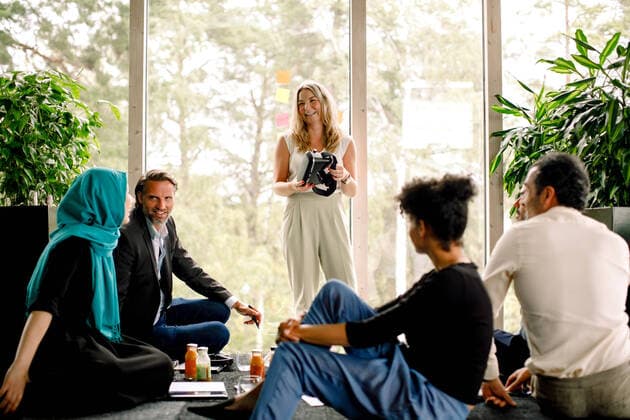 Smiling businesswoman holding virtual reality simulator while discussing with colleagues at convention center , model released, property released Copyright: xMaskotx , MA73833