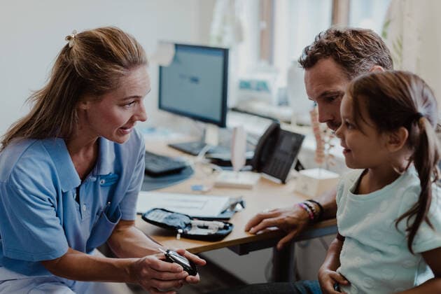 IMAGO Creative: Lokalhelden - Gesundheits- und Rettungskräfte Smiling girl looking at doctor showing glaucometer in medical examination room , model released, property released Copyright: xMaskotx , MA73893