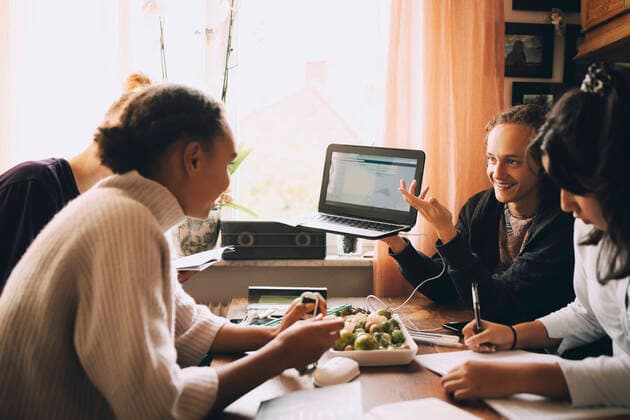 Smiling teenage boy showing laptop to friends while studying at table , model released, property released Copyright: xMaskotx , MA74396